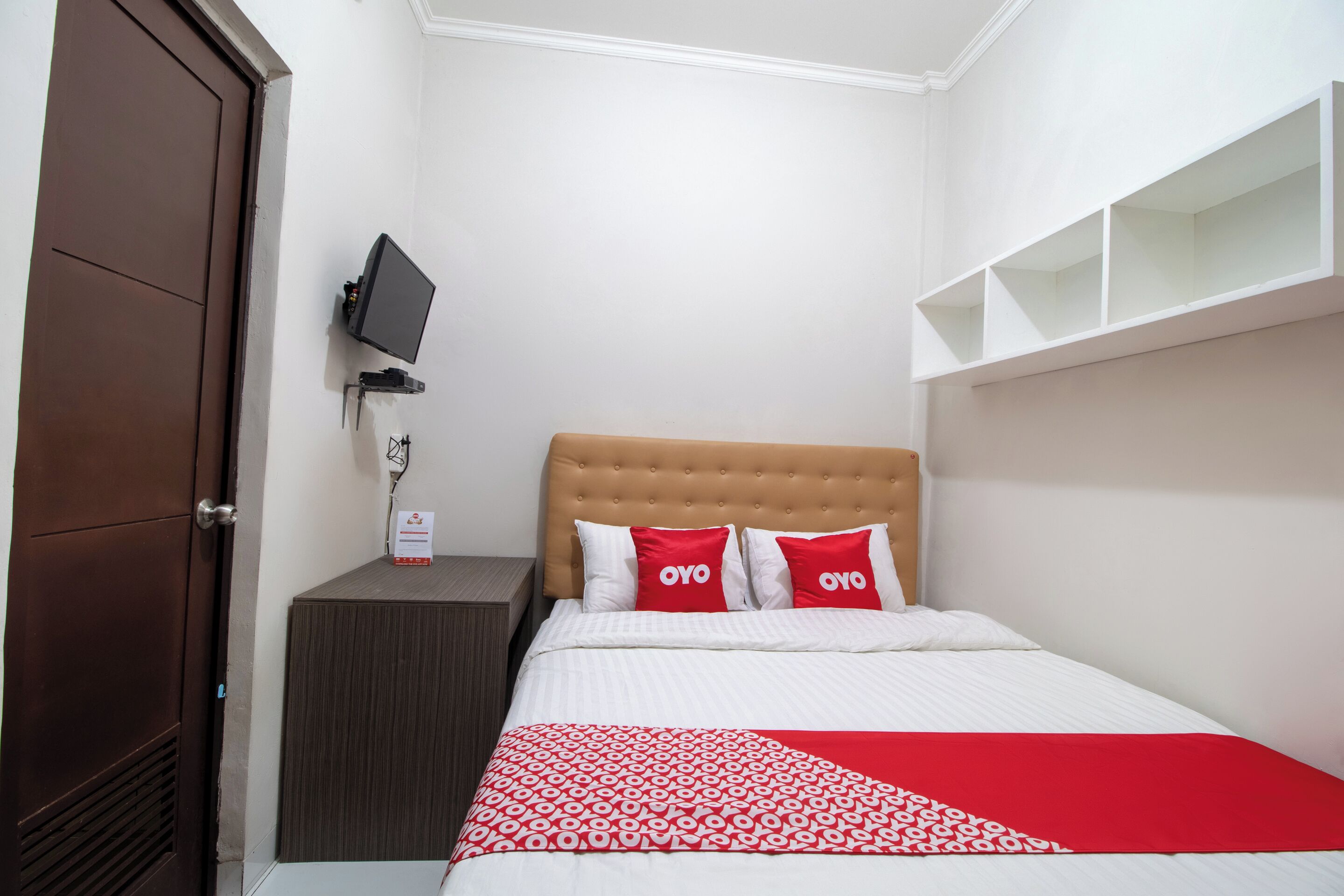 Una habitación de hotel con cama, televisor sobre un mueble, armario y estantería.