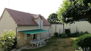 Une maison avec un toit rouge, un auvent vert et une terrasse avec des chaises blanches.