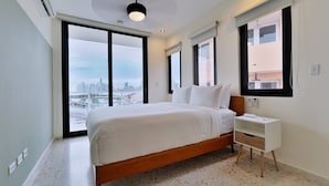 Un dormitorio moderno con vista a la ciudad, un cabecero de madera, una mesita de noche blanca y un ventanal grande.