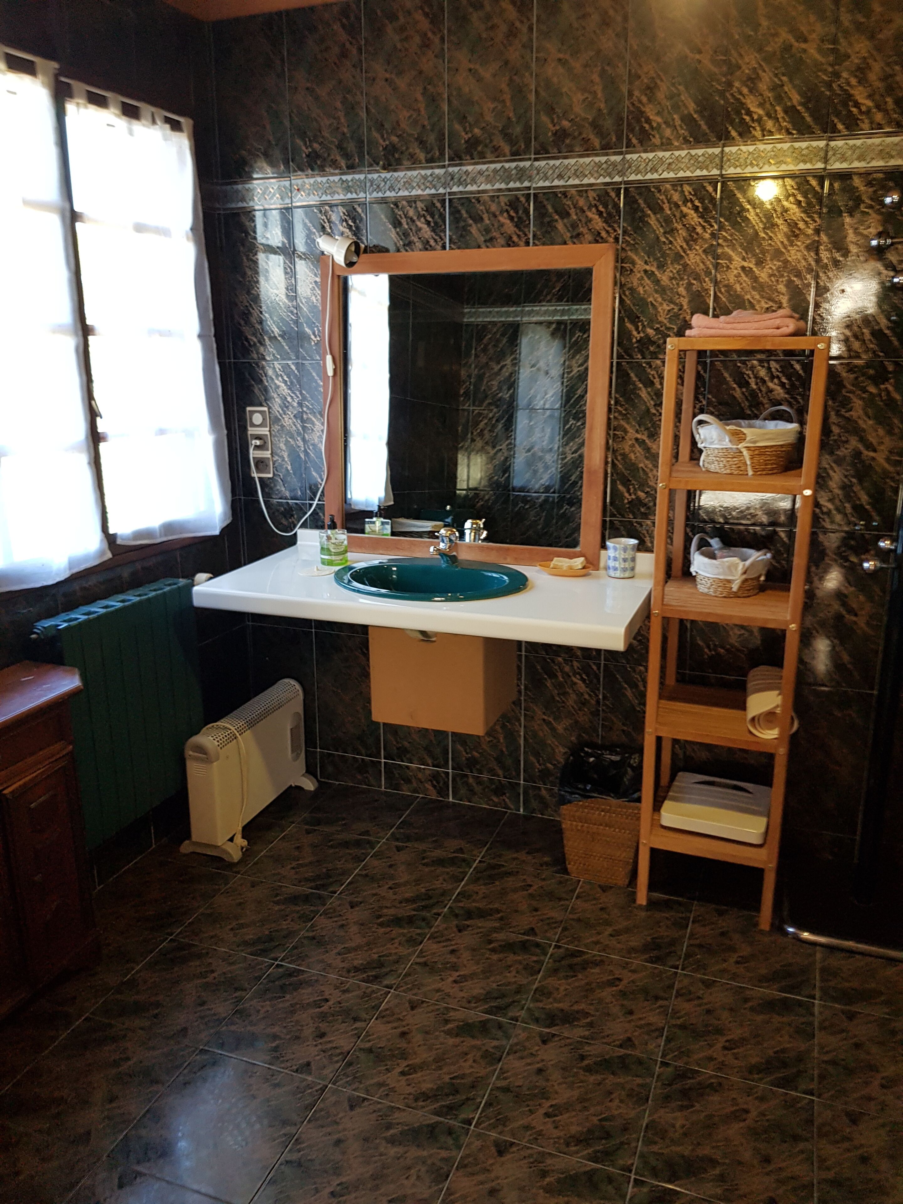 Un bagno con rivestimento in marmo, un lavandino bianco, uno specchio, un porta asciugamani e un termosifone.