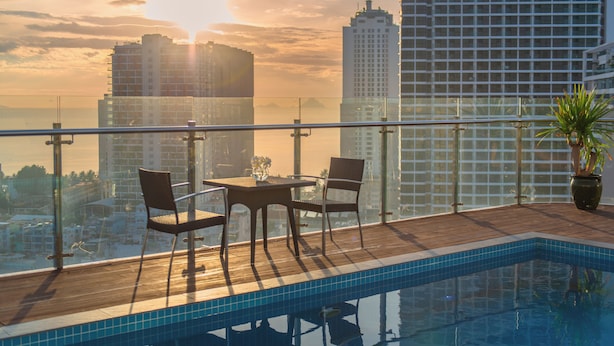A rooftop pool with a view of city buildings, a glass railing, and a table with chairs. - The Gold Coast Hotel Nha Trang (Nha Trang)