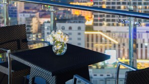 A cityscape view from a balcony with a table and chairs, a vase with flowers, and a railing. - The Gold Coast Hotel Nha Trang (Nha Trang)