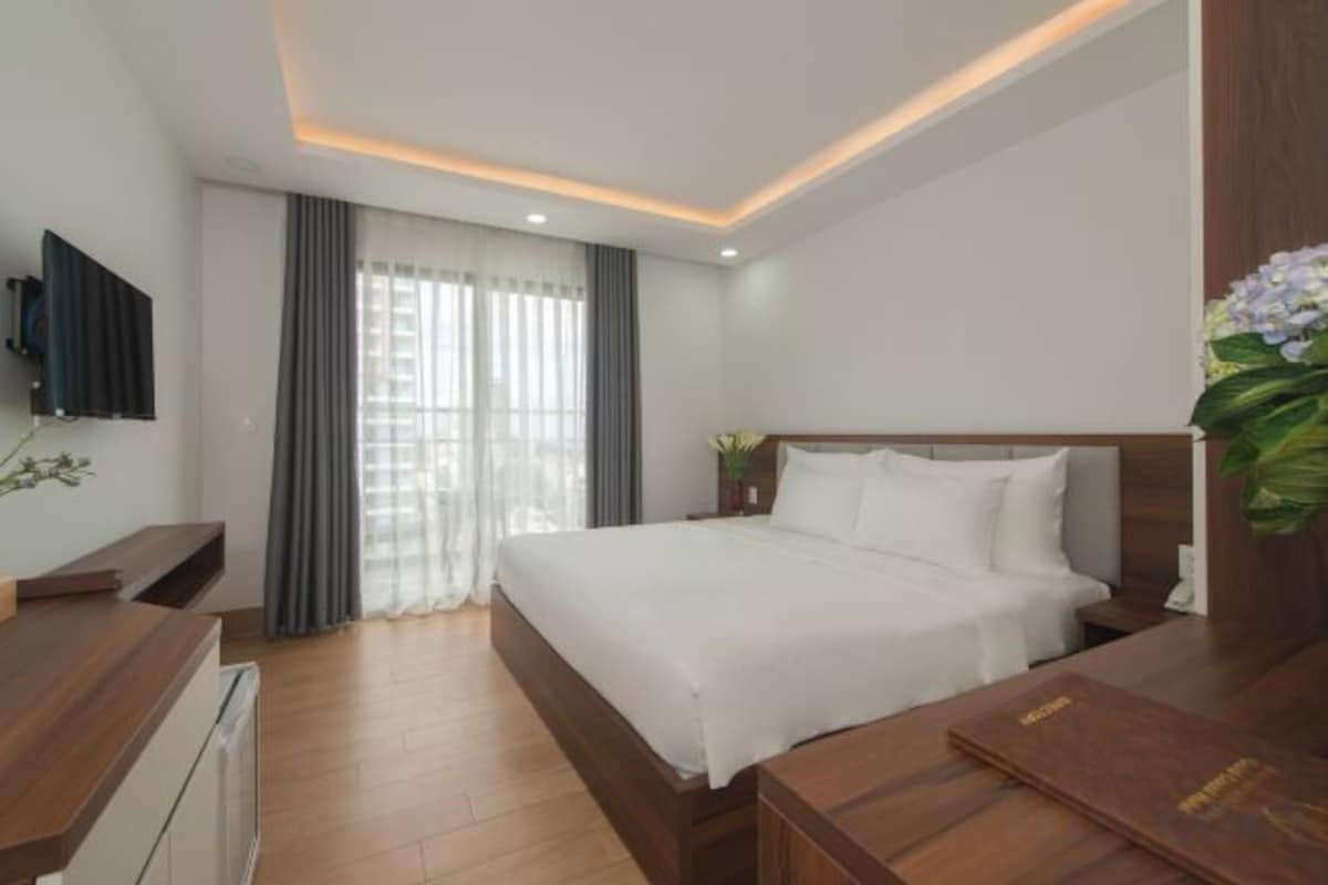 A hotel room with a bed, a desk, a television, and a window with curtains.