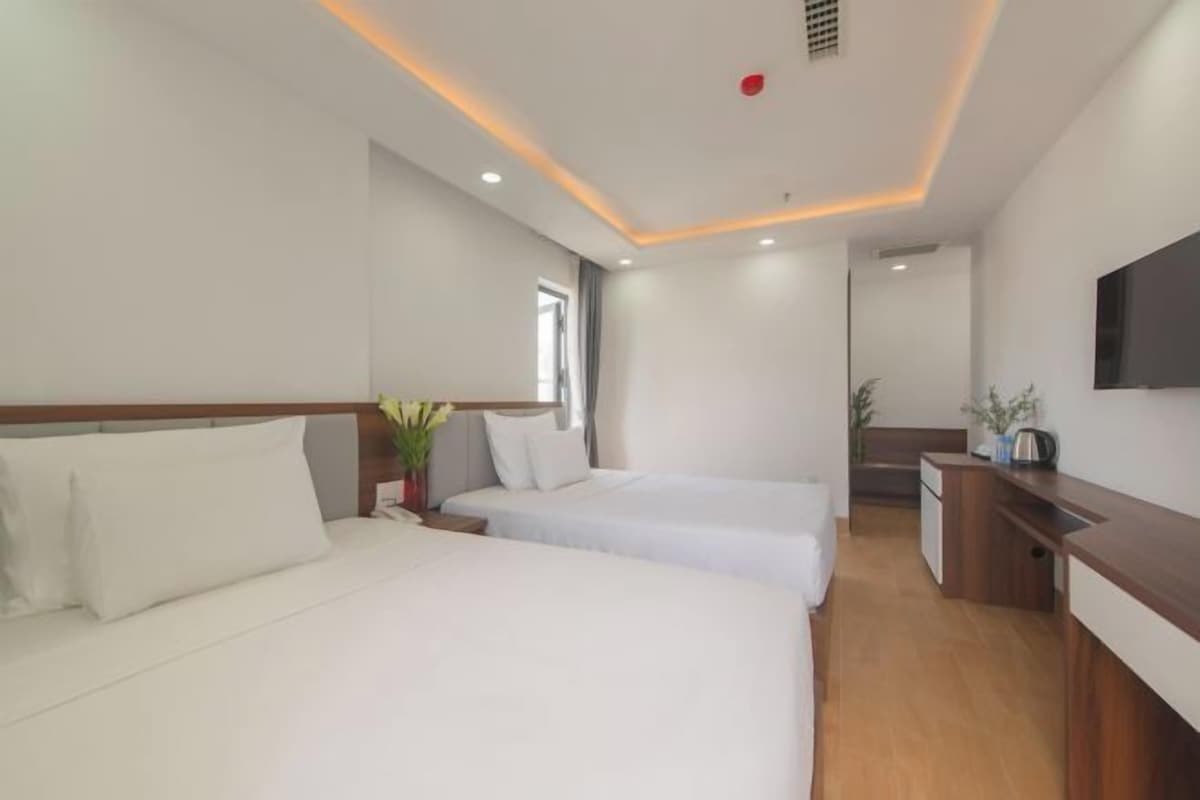 A hotel room with two beds, a desk, a TV, and a small kitchenette.