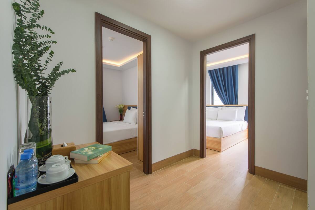 A hotel room with a wooden desk, a mirror, a bed with white bedding, and a view of a blue curtain.