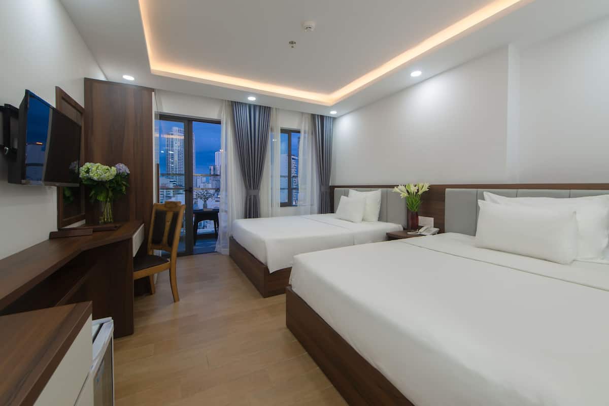 A hotel room with two beds, a desk, a chair, and a TV.