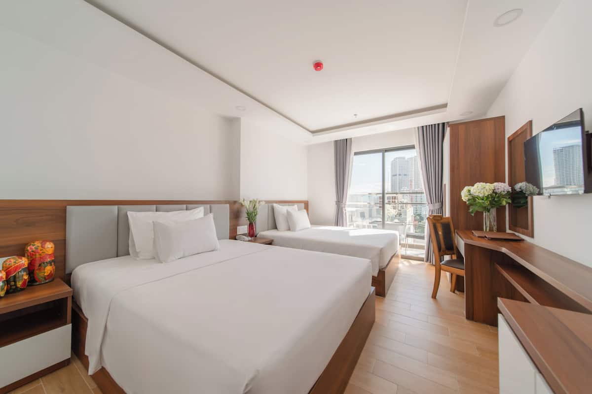 A hotel room with two beds, a desk, a chair, a TV, and a balcony with a city view.