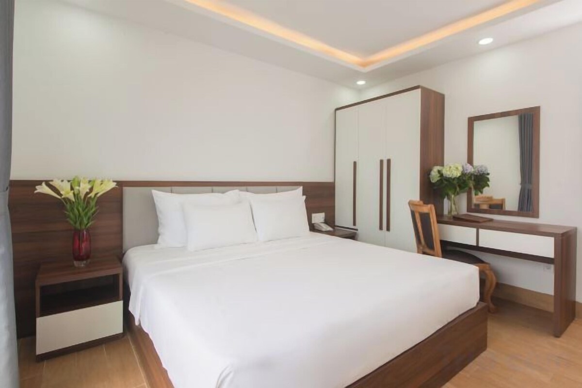 A hotel room with a large bed, bedside tables, a desk, and a mirror.
