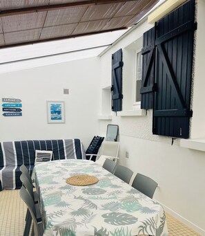 A room with a dining table, chairs, a sofa, and a view of the sea.
