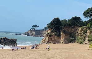 Ein Strand mit Menschen, einem Felsen und Bäumen.