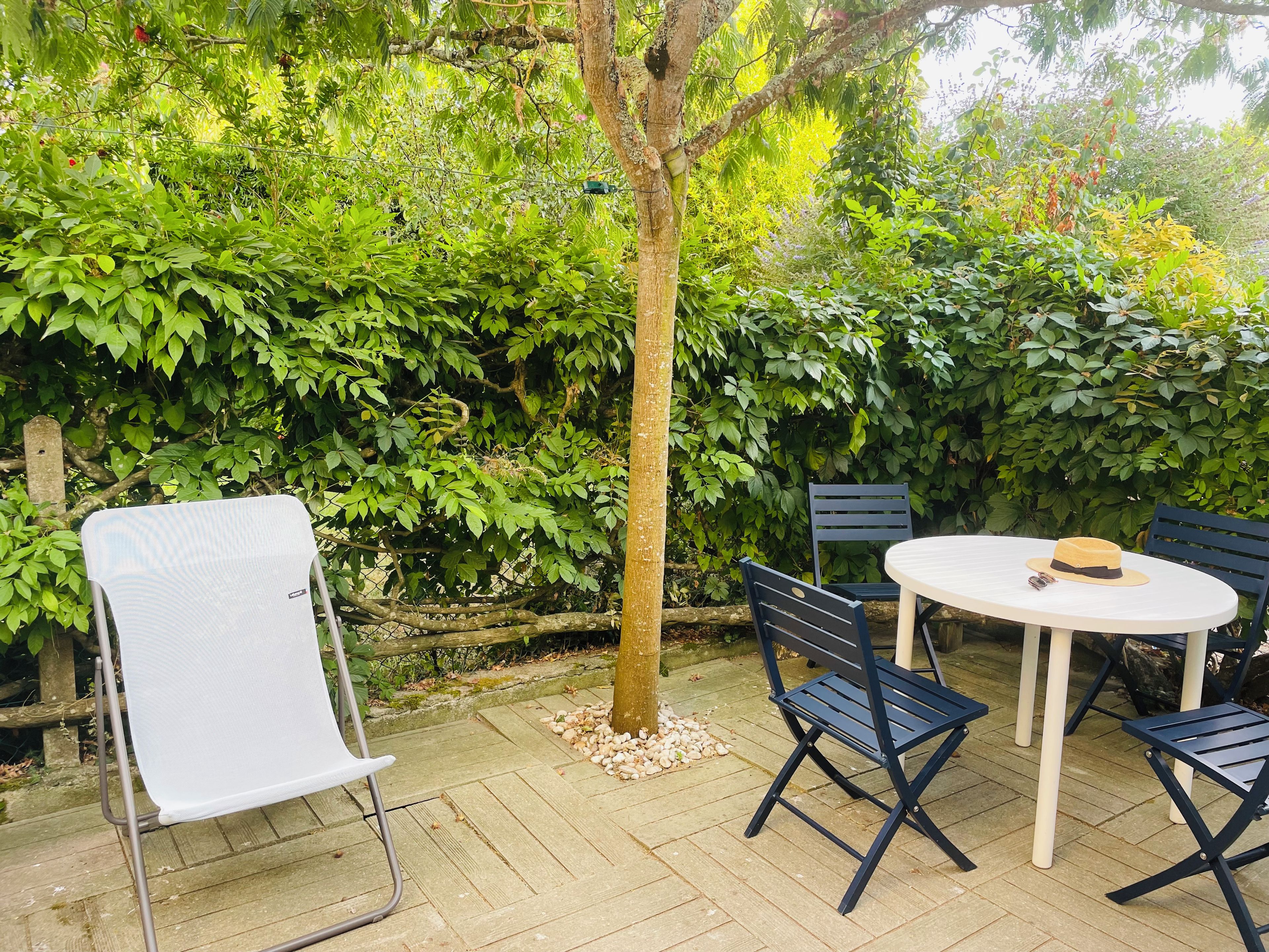 An outdoor patio with a round table, four chairs, and a small tree.