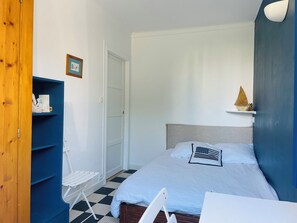 Een slaapkamer met een bed, een stoel, een plank met decoratieve spullen en een deur.