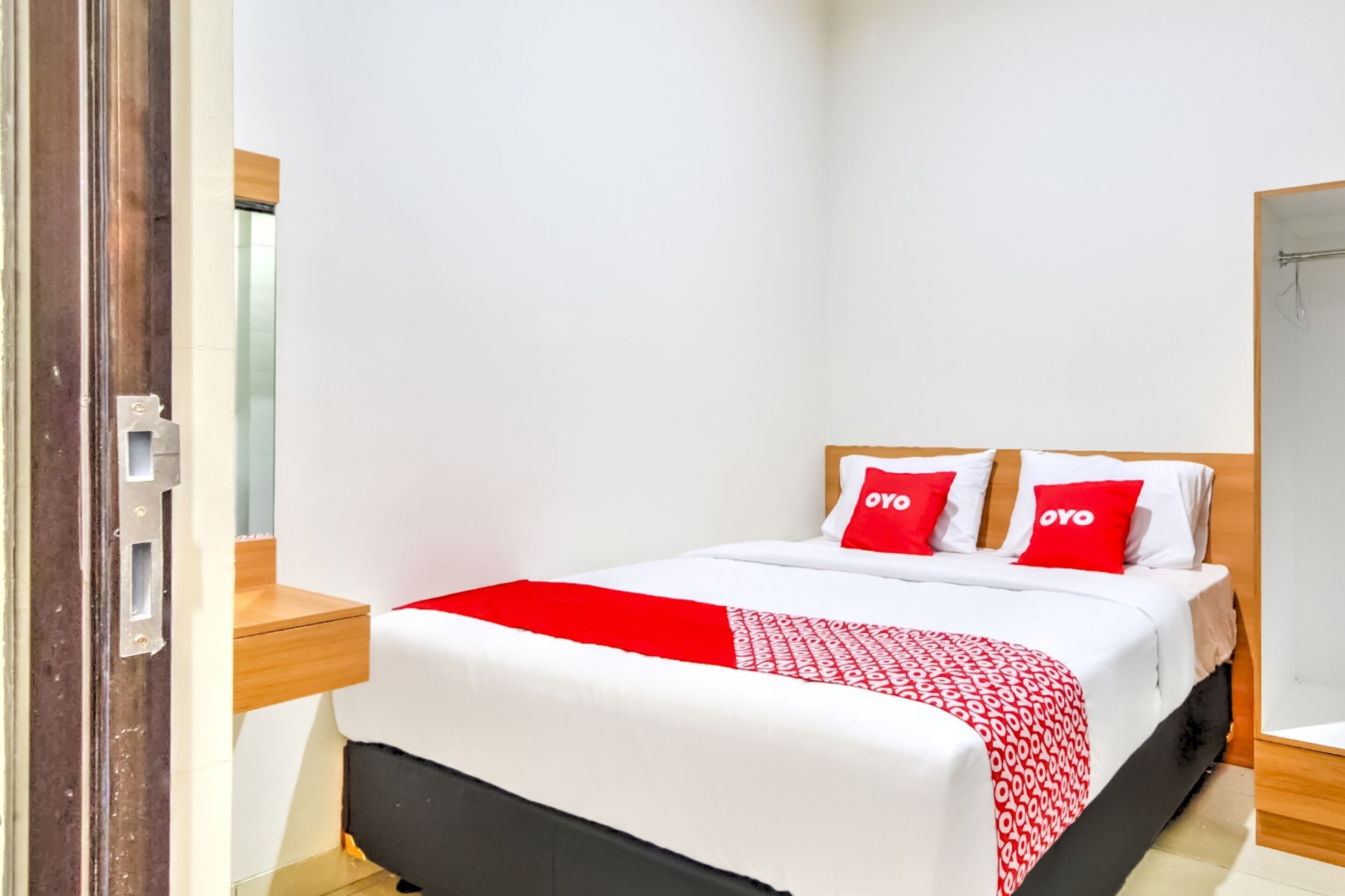 A neatly made bed with a red and white patterned bedspread, two red pillows with the word "OYO" on them, and a wooden headboard.