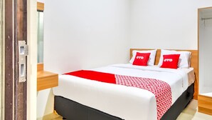 A neatly made bed with a red and white patterned bedspread, two red pillows with the word "OYO" on them, and a wooden headboard. - OYO 3346 Rukos Colombus G5 (Karawang)