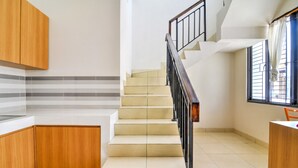 A kitchen with wooden cabinets, a tiled floor, and a staircase with a black railing. - OYO 3346 Rukos Colombus G5 (Karawang)