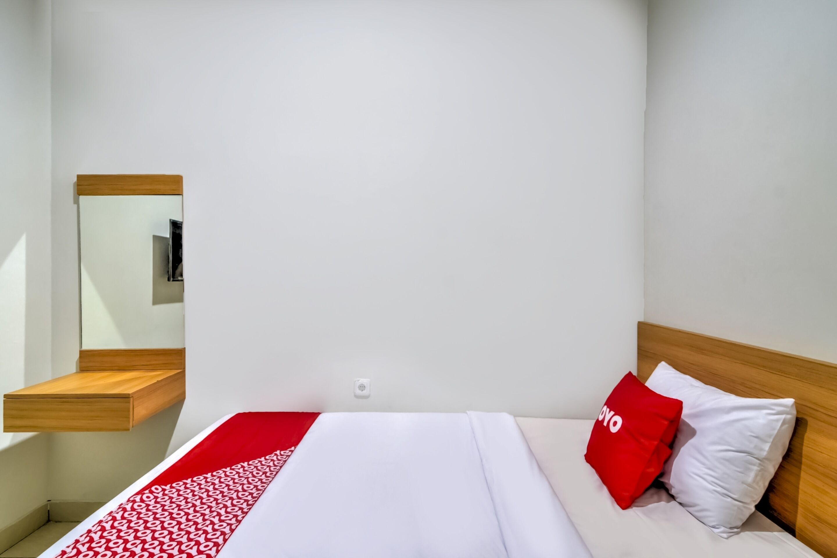 A hotel room with a bed, a wooden nightstand, a mirror, and a red and white patterned bedspread.