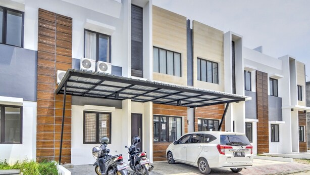 A modern multi-story residential building with a covered entrance, two motorcycles parked outside, and a white car parked in front. - OYO 3346 Rukos Colombus G5 (Karawang)