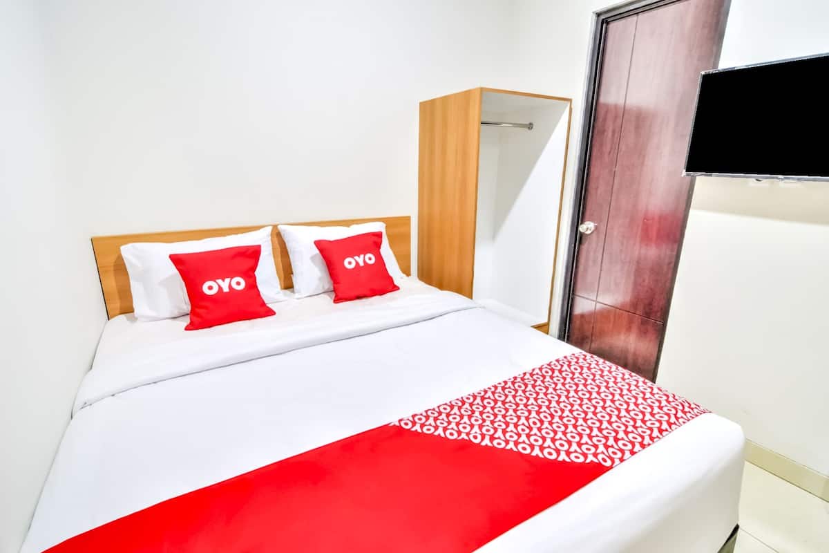 A hotel room with a bed, two red pillows with "OYO" branding, a wooden wardrobe, and a TV mounted on the wall.