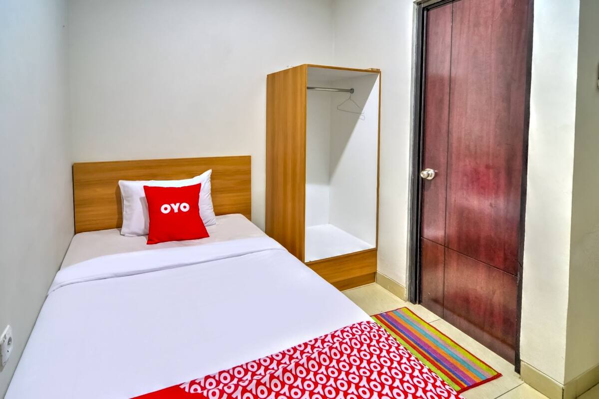 A hotel room with a bed, a wooden wardrobe, a door, and a colorful rug.