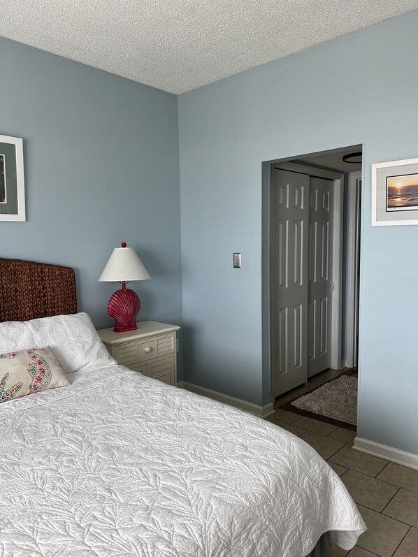 A bedroom with a bed, a nightstand, a lamp, and a door leading to another room. - Direct Ocean Front! Beautiful Cabana End Unit GROUND FLOOR...rare find! (Murrells Inlet)