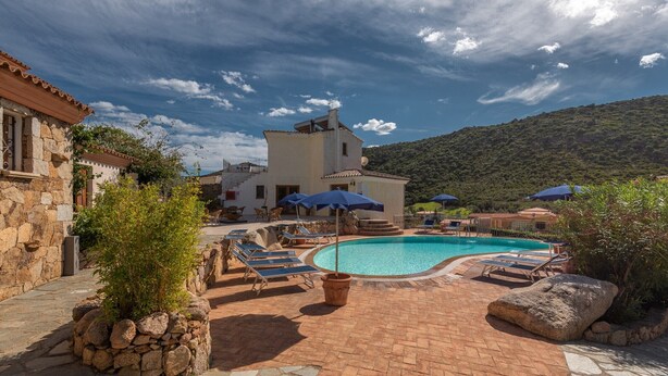 A pool area with lounge chairs and umbrellas, surrounded by stone walls and vegetation. - Stunning Residence Bouganvillage Studio (Budoni)