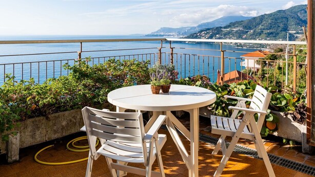 A terrace with a round table and two white chairs, overlooking a coastal view with mountains in the distance. - Beautiful apartment for 3 guests with WIFI and terrace (Ventimiglia)