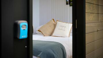 Un dormitorio con cama, almohadas, una colcha y un termostato en la pared.