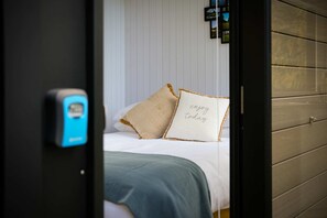Une chambre à coucher avec un lit, des oreillers, une couverture et un thermostat fixé au mur.
