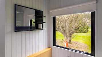 A bathroom with a large window, a mirror, and a shelf with a cup and a tissue.