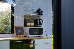 Un comptoir de cuisine avec un micro-ondes blanc, une machine à café et une étagère contenant de la verrerie et une bouteille bleue. Une pancarte indique : « Bienvenue au Ryan’s Ranch Norman & Boone. »