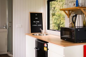 Une cuisine avec un plan de travail en bois, un évier en acier inoxydable, un micro-ondes noir et une pancarte sur laquelle on peut lire : « BONJOUR ET BIENVENUE AU LYDIA’S LODGE. »
