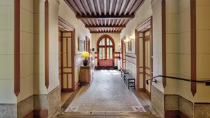 Un pasillo con techo de madera, un banco, una lámpara y una puerta con ventana.