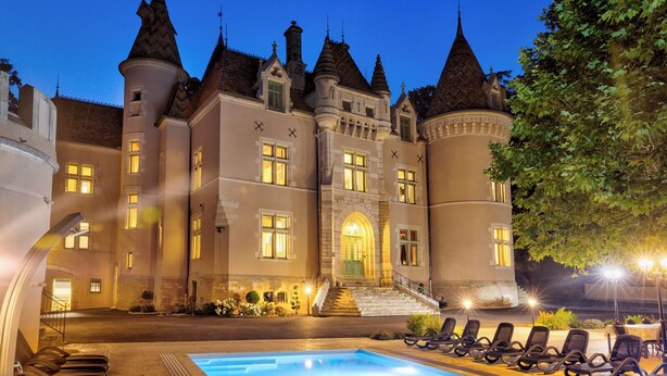 Un edificio de estilo castillo con piscina y sillas de descanso.