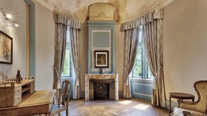 Una habitación con escritorio de madera, una silla, chimenea y cortinas con estampado.