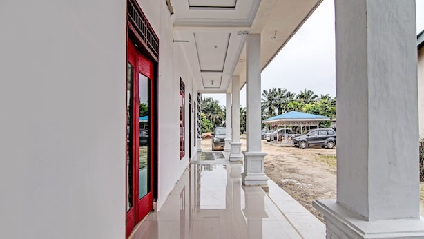 A clean, white corridor with red doors, leading to a covered area with a blue umbrella.