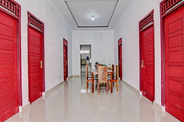 A hallway with red doors, a dining area with wooden chairs and a table, and a ceiling light. - Hotel O Wisma Cendana Syariah Near PASAR FLAMBOYAN (Tapung)