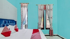 A bedroom with a blue headboard, white bedding, red pillows, and patterned curtains.