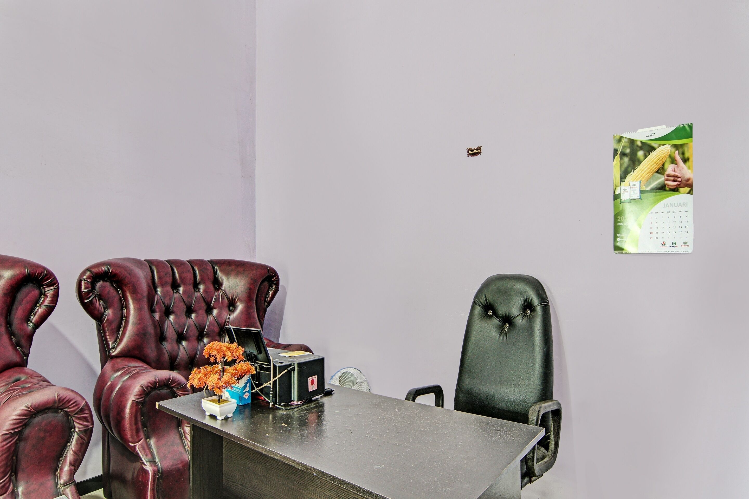 A conference room with a dark leather chair, a white table, and a calendar on the wall.