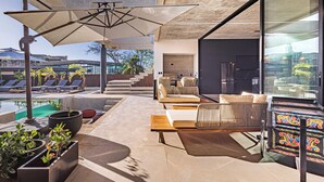 A modern outdoor lounge area with a pool, lounge chairs, and a large umbrella. - Casa Uana, luxury new home in gated community, private pool, steps to the beach (Tamarindo)