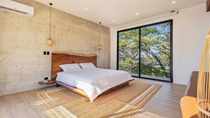 A modern bedroom with a large bed, a concrete wall, and a large window. - Casa Uana, luxury new home in gated community, private pool, steps to the beach (Tamarindo)