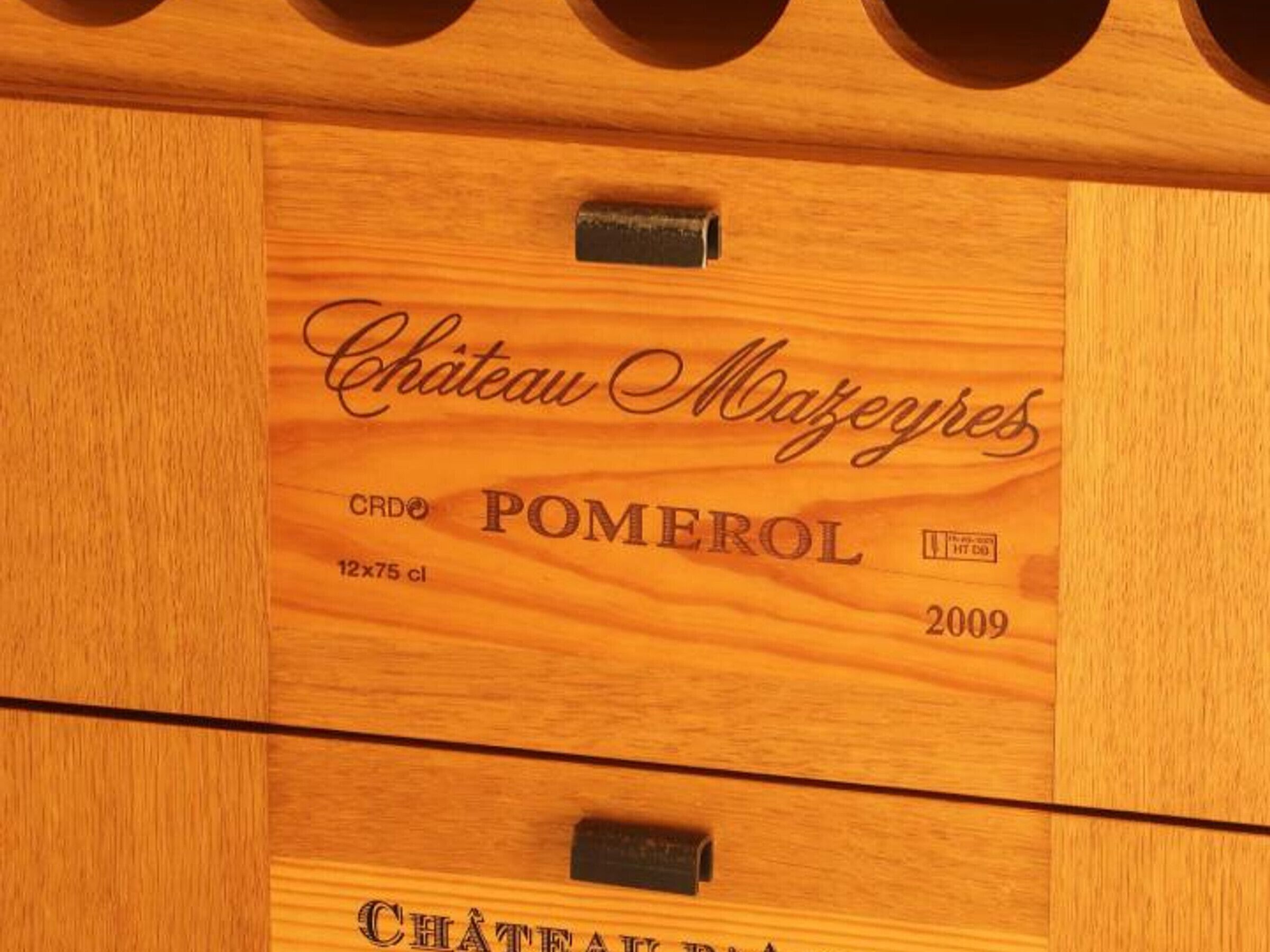 Een houten paneel met in reliëf de tekst: “Château Mažeires,” “CRD,” “POMEROL,” “12x75 cl” en “2009.”