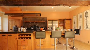 A modern kitchen with wooden cabinetry, a central island with bar stools, and a dining area with a table and chairs.