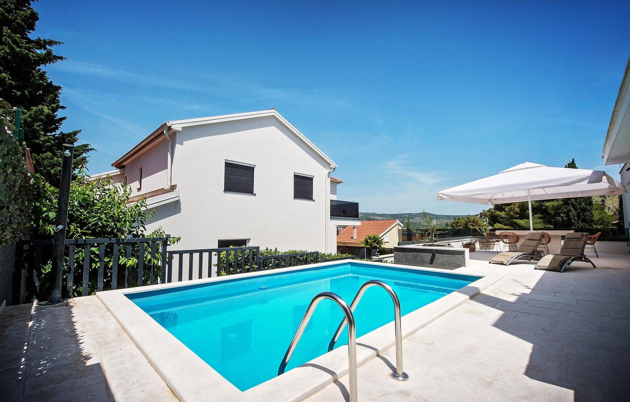 A modern two-story house with a swimming pool, outdoor seating, and a view of the surrounding landscape.