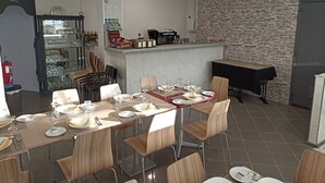A dining area with a long table set for a meal, a kitchen area with a brick wall, and a WC sign on the left.