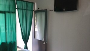 A room with two beds, a TV mounted on the wall, and green curtains.