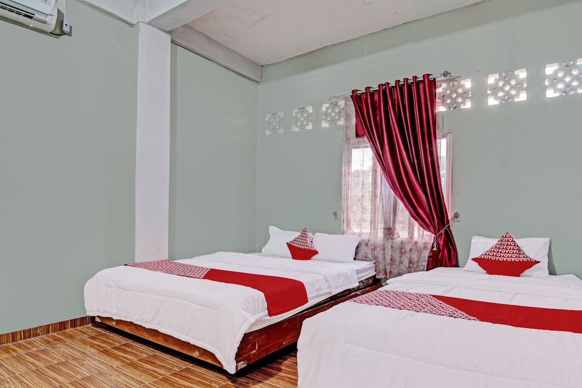 A hotel room with two beds, a window with a curtain, and a wall-mounted air conditioner.