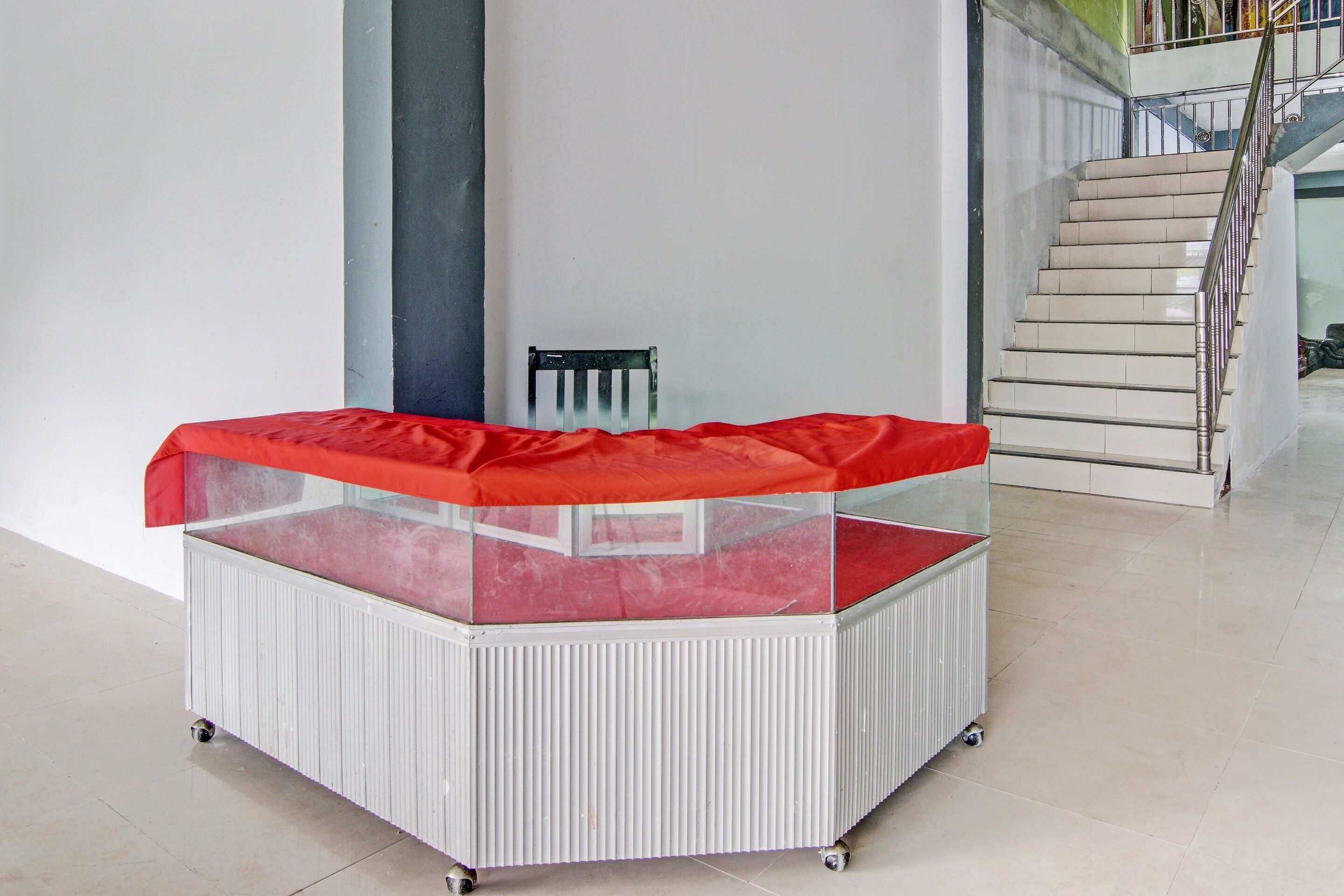 A corner booth with a red canopy, white ribbed base, and wheels, located in a modern interior with a staircase in the background.