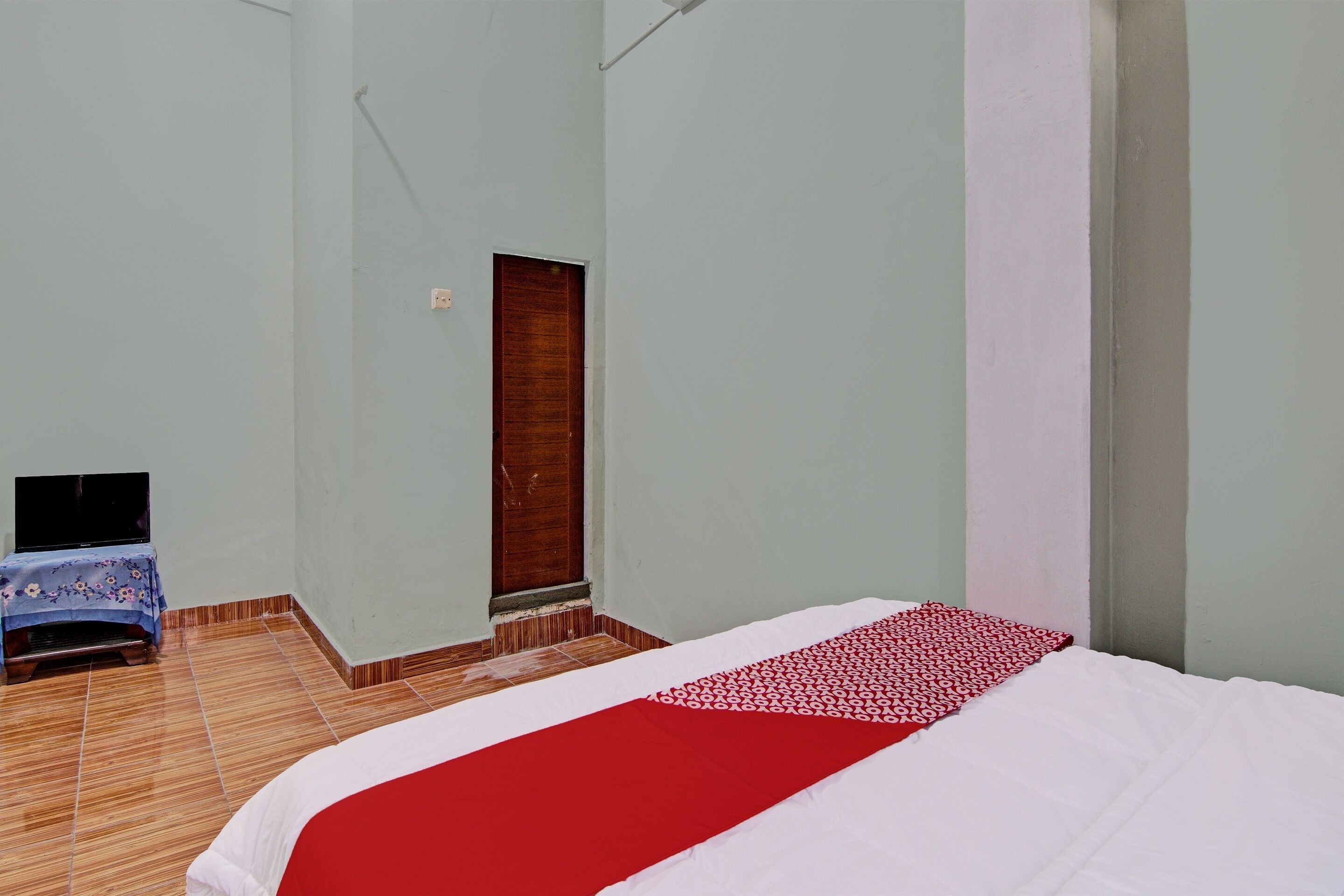 A room with a bed, a wooden door, a small table with a TV, and a tiled floor.