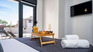 A modern hotel room with a bed, a bedside table with a tray of breakfast, a TV mounted on the wall, and a view of the outside. - Luxurious home in Zadar (Zadar)