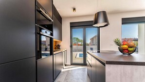 A modern kitchen with a built-in oven, a coffee machine, and a fruit bowl on the counter. - Luxurious home in Zadar (Zadar)